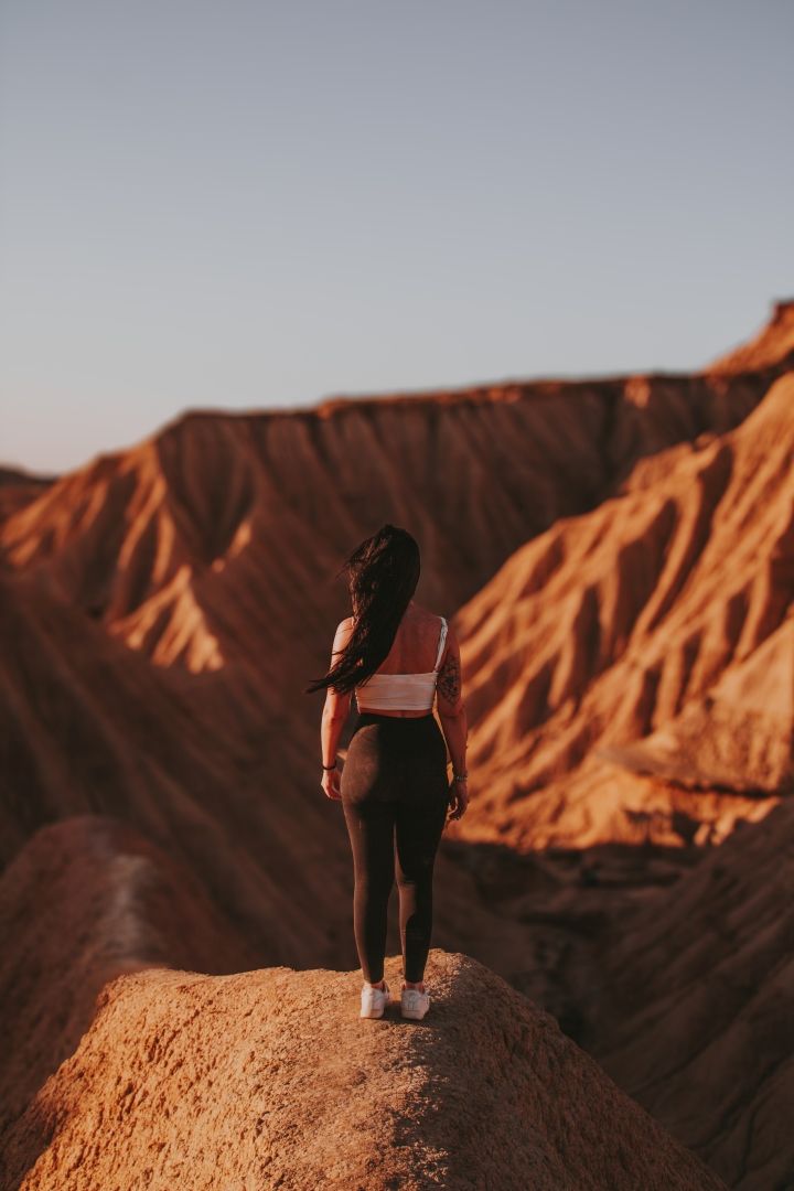 montañas deserticas y chica de espalda en primer plano con pelo largo negro mirando a las montañas