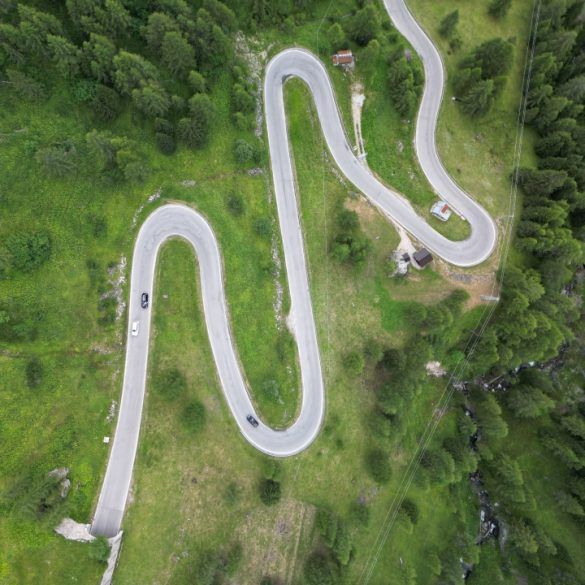 fotografia aerea de carretera de curvas con bosque alpino y prado verde alrededor