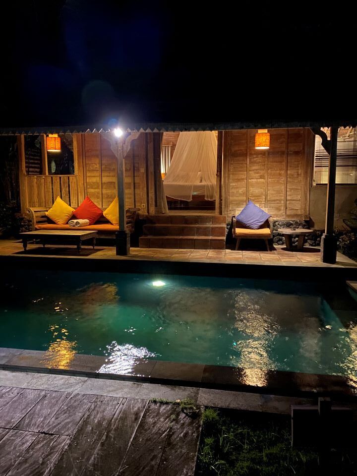 vista de caseta de madera desde fuera con luces de noche y piscina delante