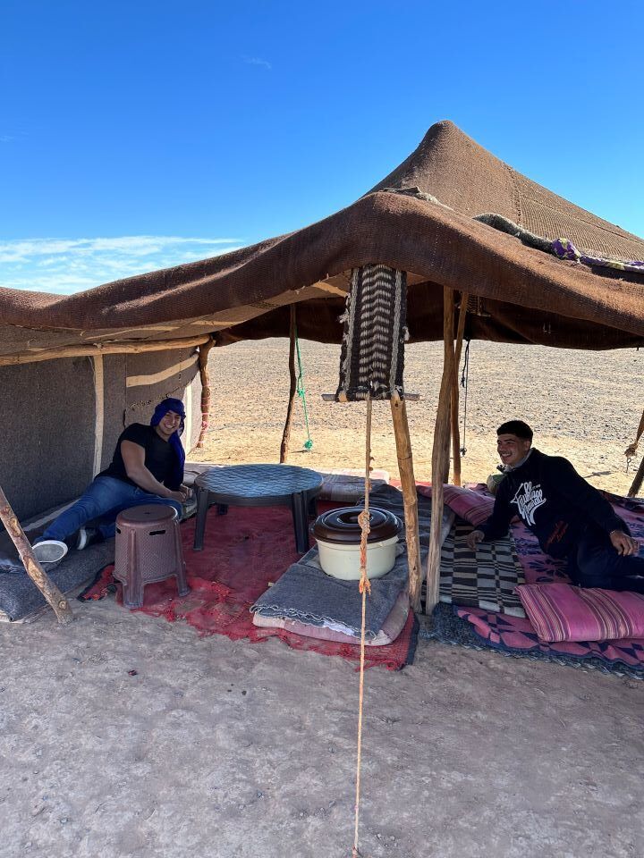 viajar a Marruecos aldea berebere, toldo de telas y dos chicos tumbados debajo encima de mantas en merzouga