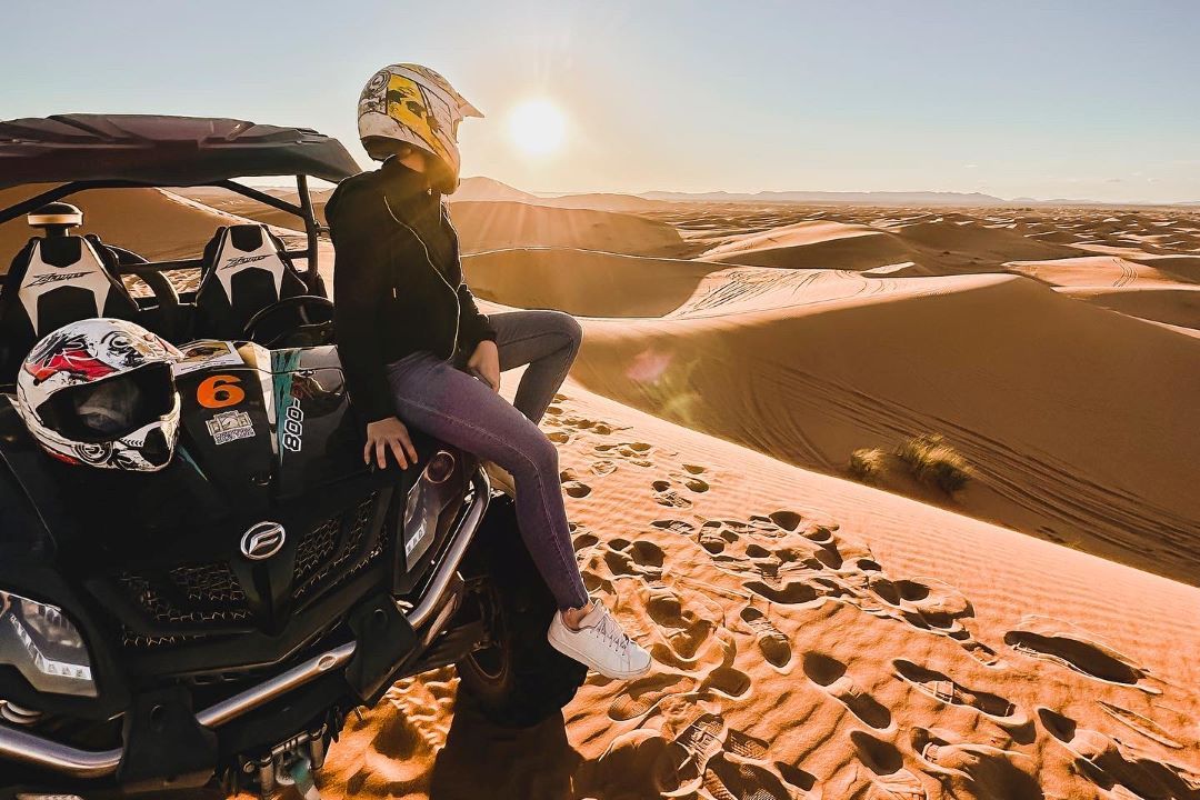 buggy en el desierto y chica con casco miranod hacia el sol del atardecer