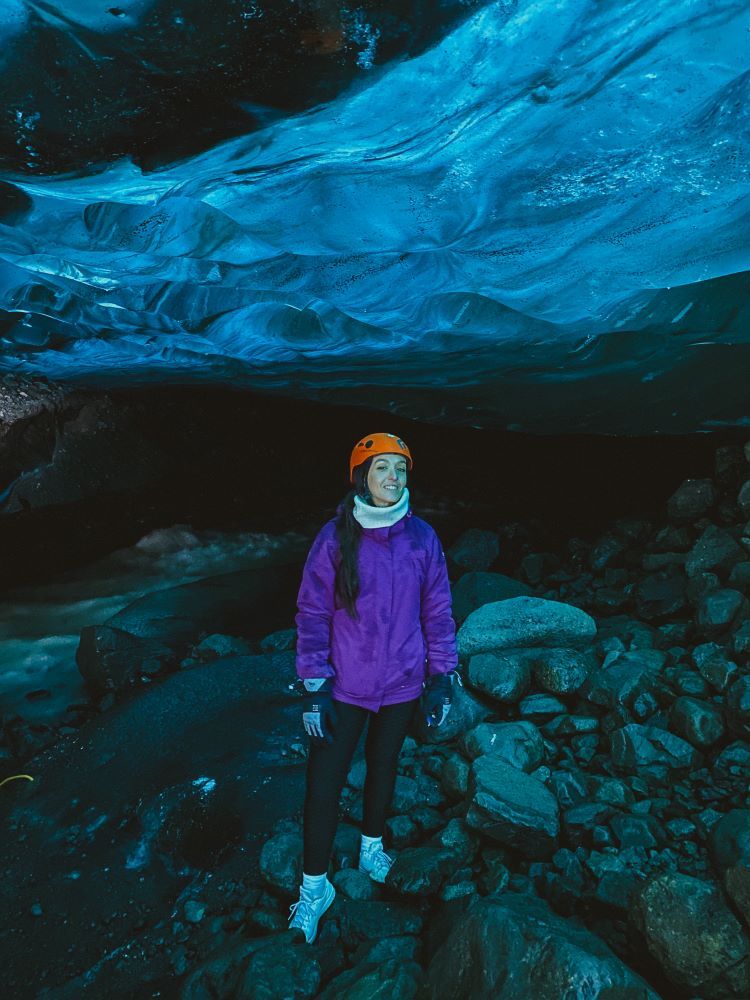 cueva de hielo azul en la parte superior y persona posando de frente con chaqueta liila y casco naranja