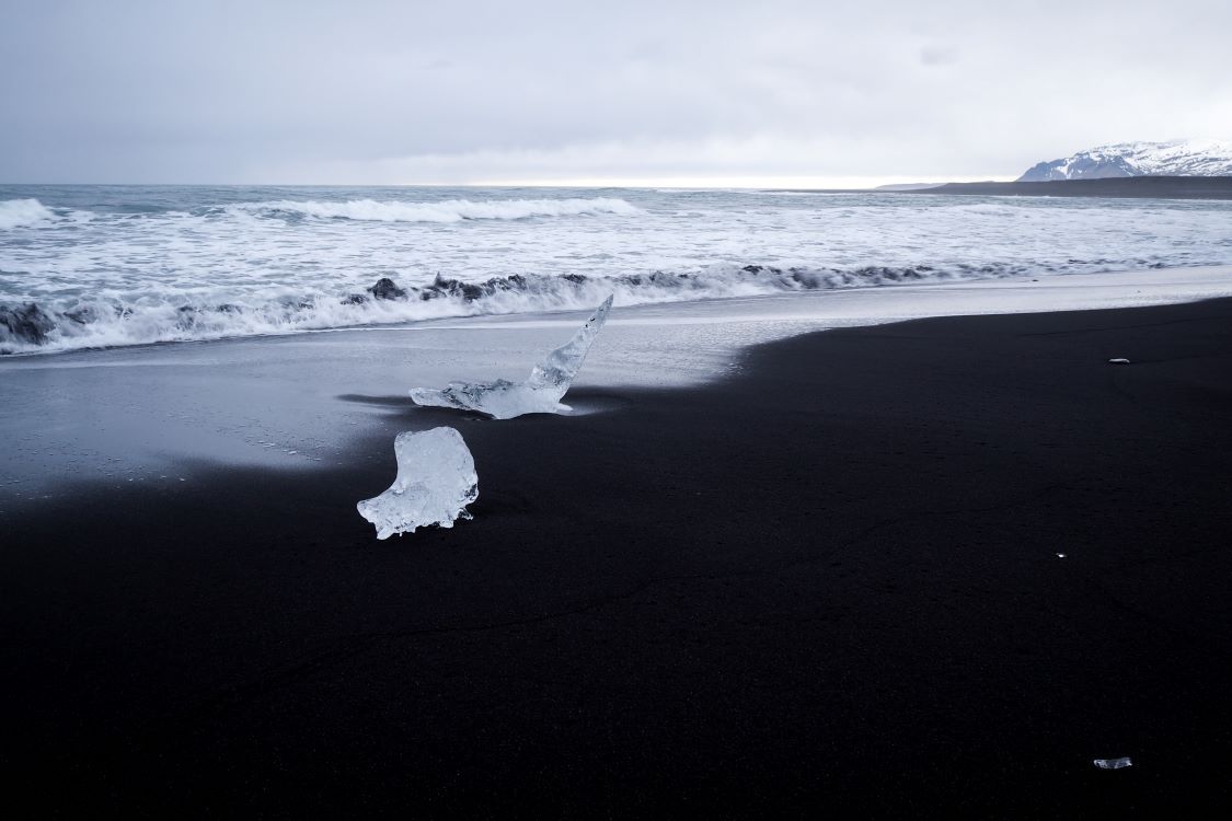 playa negra en islandia con dos trozos de hielo y el mar de fondo
