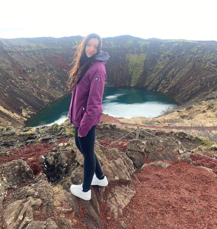 crater lleno de agua y en medio chica con chaqueta lila posando y mirando a la cámara