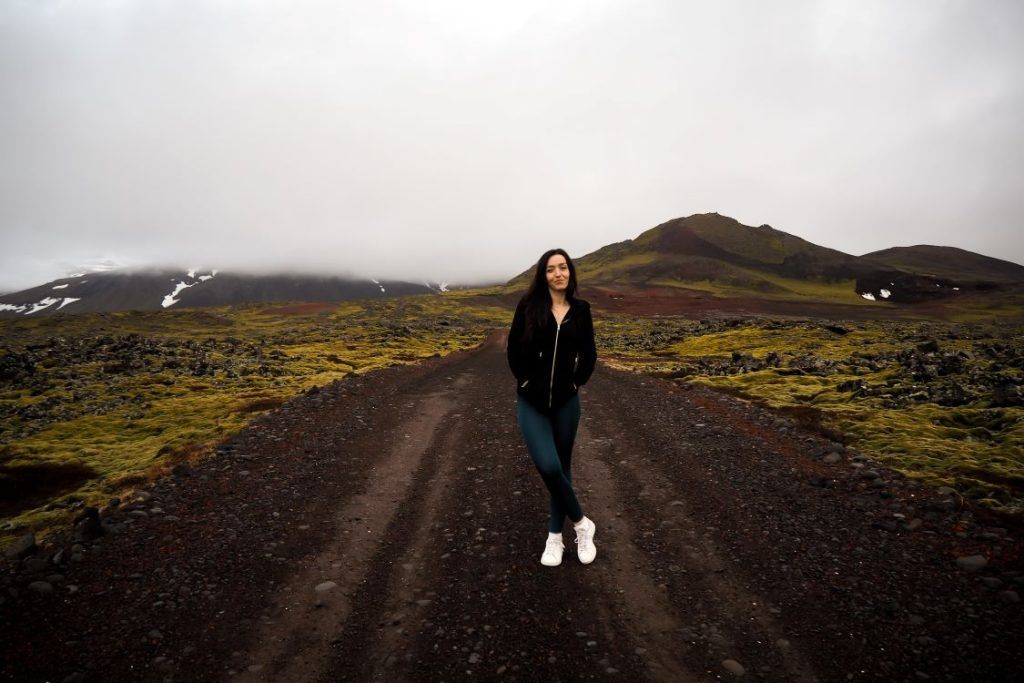 camino de tierra oscuro con chica en medio posando de frente con chaqueta negra y deportivas blancas