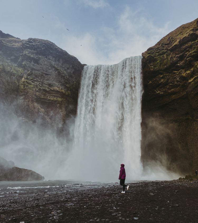 cascada vista desde abajo de frende con persona con chaqueta lila caminado hacia la izquierda de lejos
