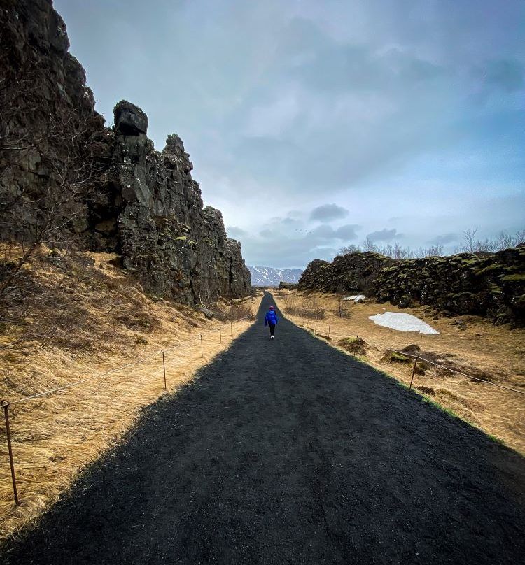 camino recto de tierra negra y acantilados de piedra a los lados que al fondo se ve una persona con chaqueta azul oscuro caminar de espaldas