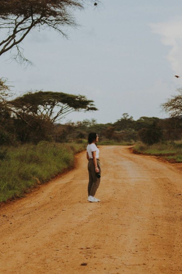 chica de lado mirando a la derecha en camino de tierra y arboles de la sabana alrededor