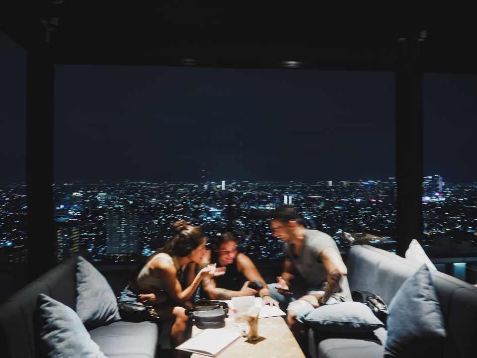 3 personas observando un menú riéndose con un pequeño desenfoque y de fondo vistas de una ciudad de noche