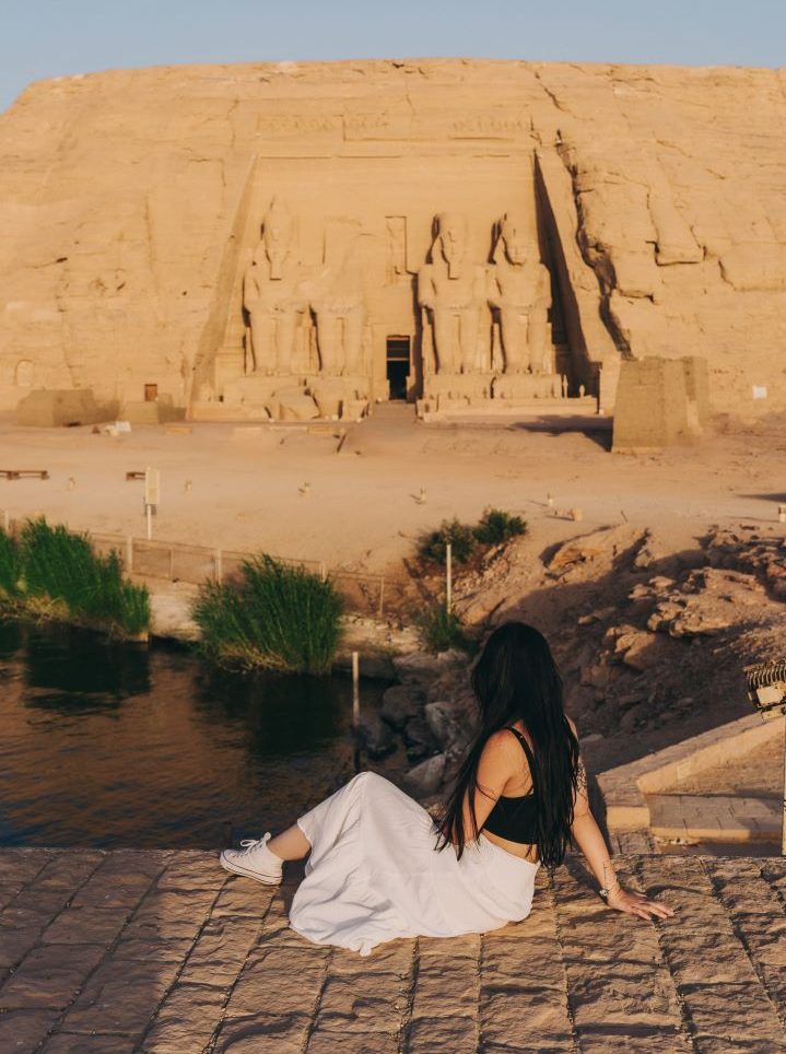 templo egipcio de fondo y chica sentada en en el suelo con una entrada del rio en un lado