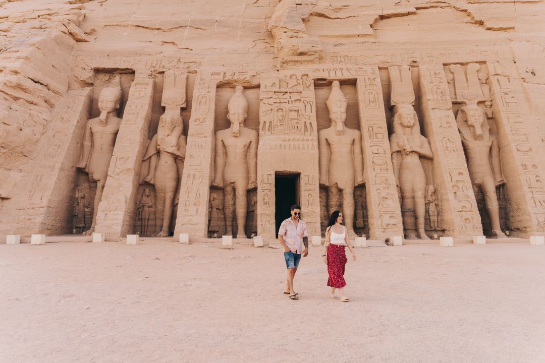 templo egipcio de fondo y una pareja andando mirando hacia la derecha sonriendo