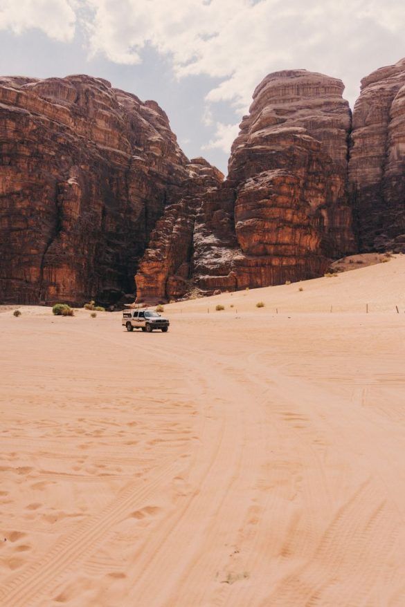 paisaje desierto con montañas de roca de fondo y un jeep parado en la arena