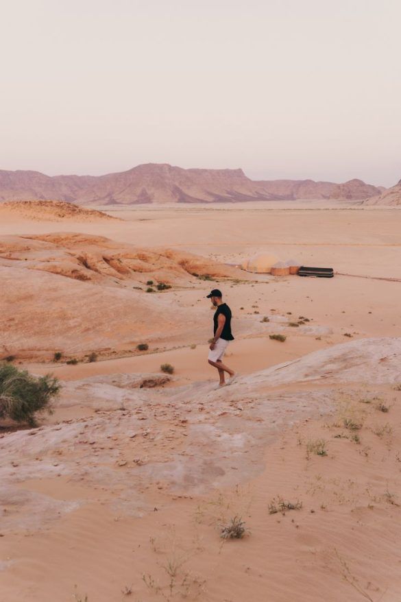 chico caminado hacia la izquierda bajando por una montaña de piedra en un desierto de arena