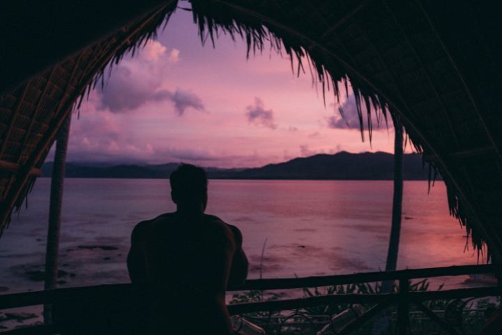 chico miradno desde un cabaña a contraluz un atardecer de colores lilas