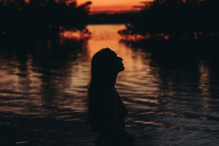 silueta chica a contraluz de un atardecer de tonos naranjas y el mar del fondo