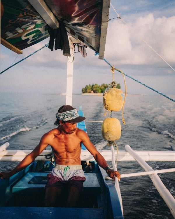filipino en una barca sin camiseta con una isla de fondo