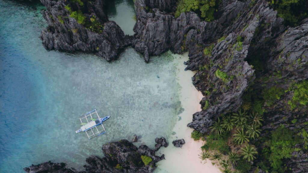 vista aerea de playa de arena blanca con vegetacion y piedra negra con barco amarrado